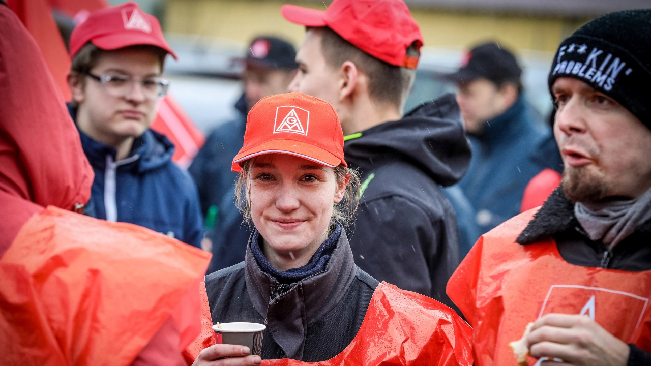 Junge Frau mit einem Kaffeebecher, Warnweste und IG Metall-Kappe.