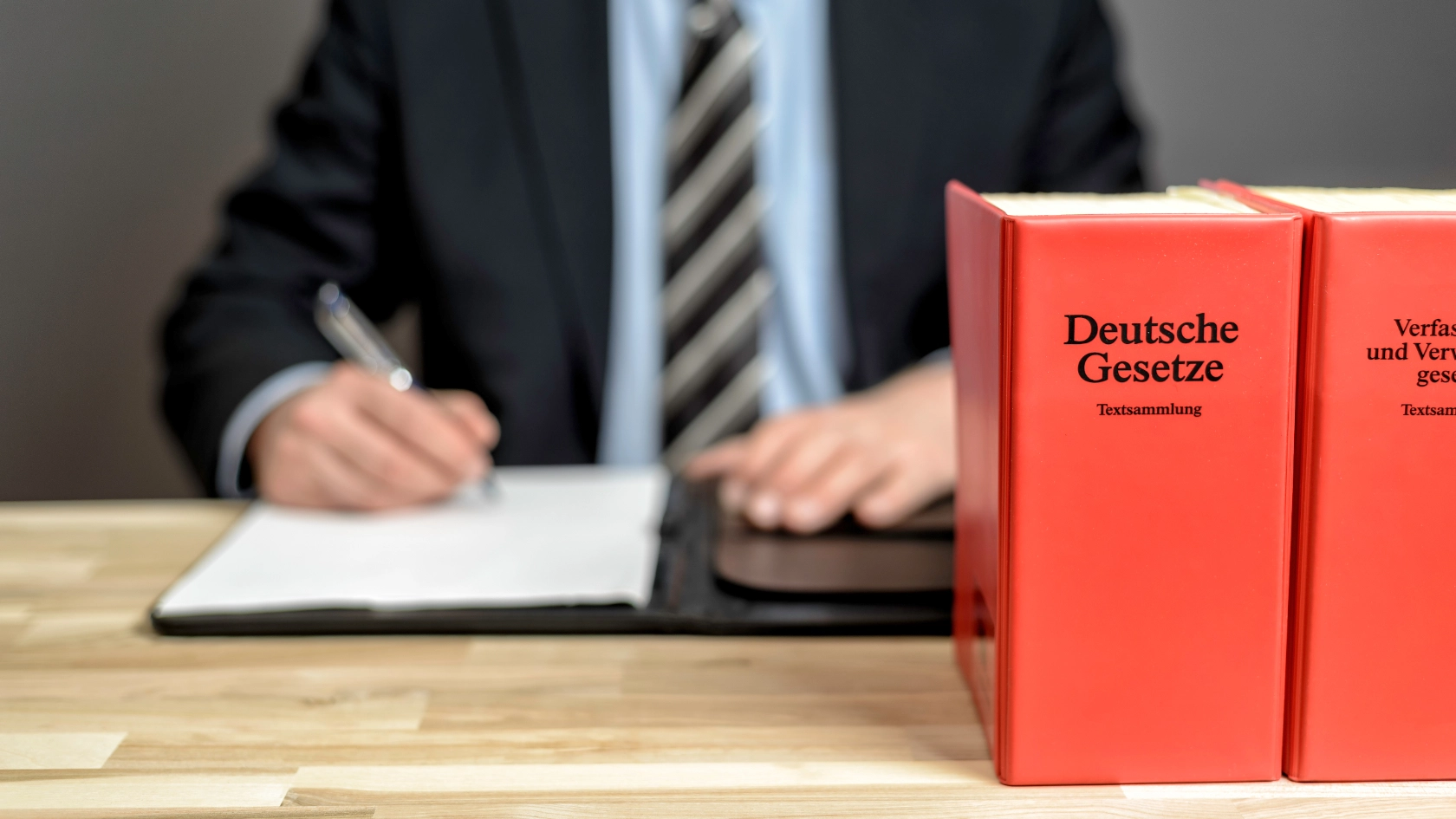 Ein Anwalt sitzt an seinem Schreibtisch, im Vordergrund sieht man deutsche Gesetzbücher