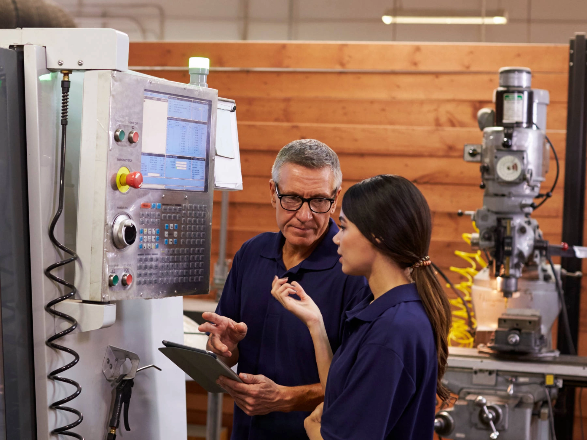 Ein Ausbilder und eine Auszubildende stehen vor einer Maschine.