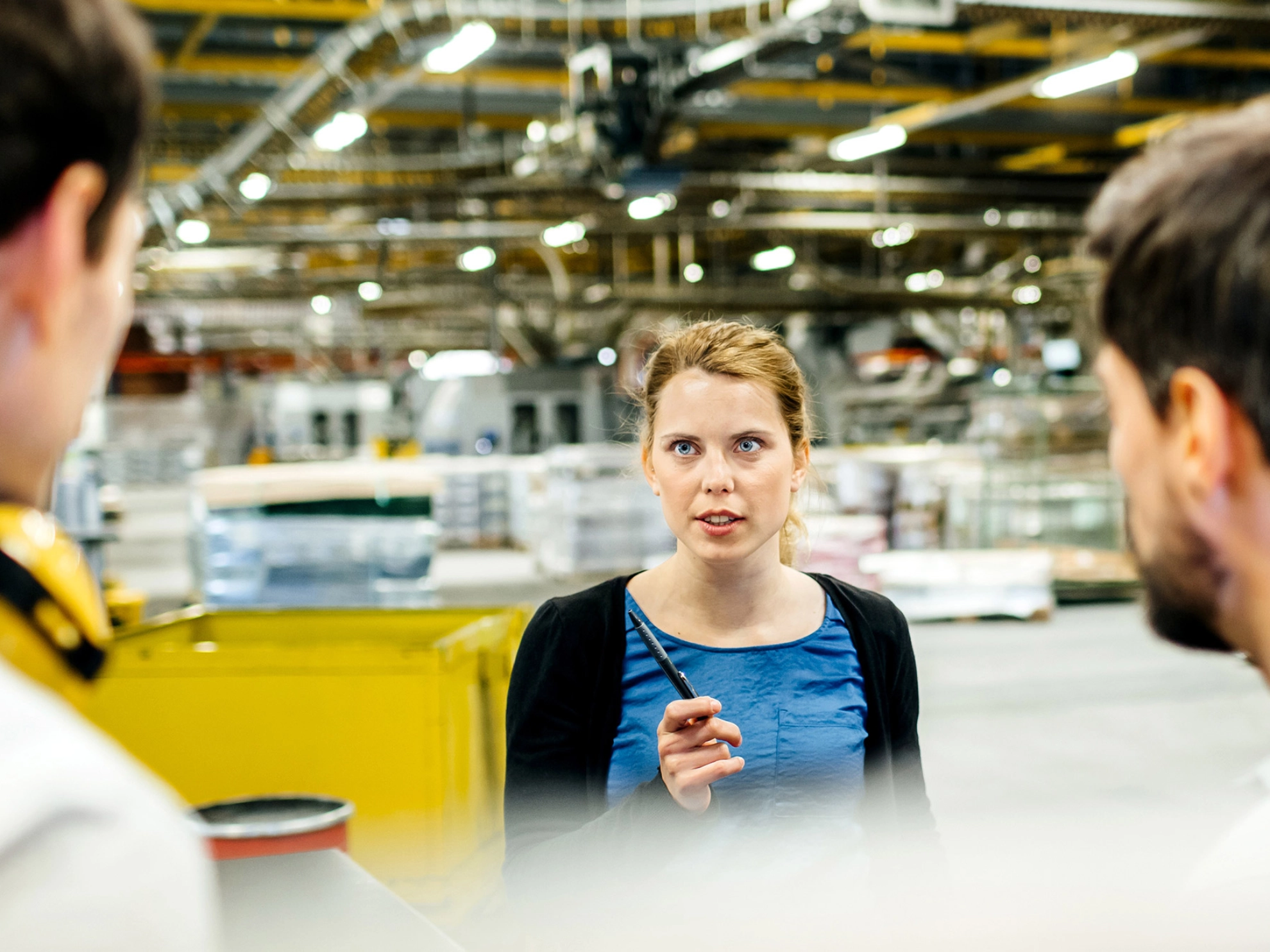 Eine Frau spricht mit zwei Männern an einer Produktionslinie.