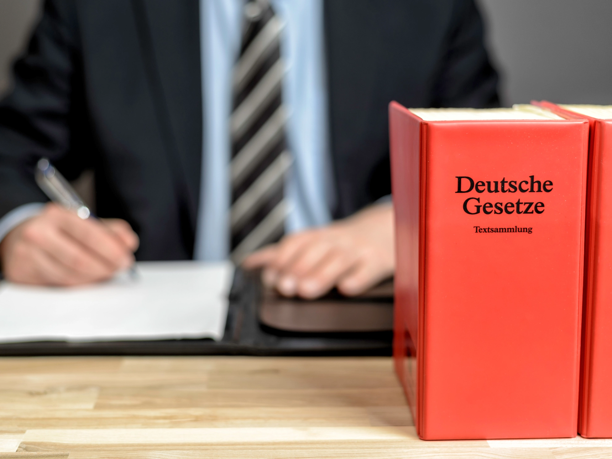 Ein Anwalt sitzt an seinem Schreibtisch, im Vordergrund sieht man deutsche Gesetzbücher